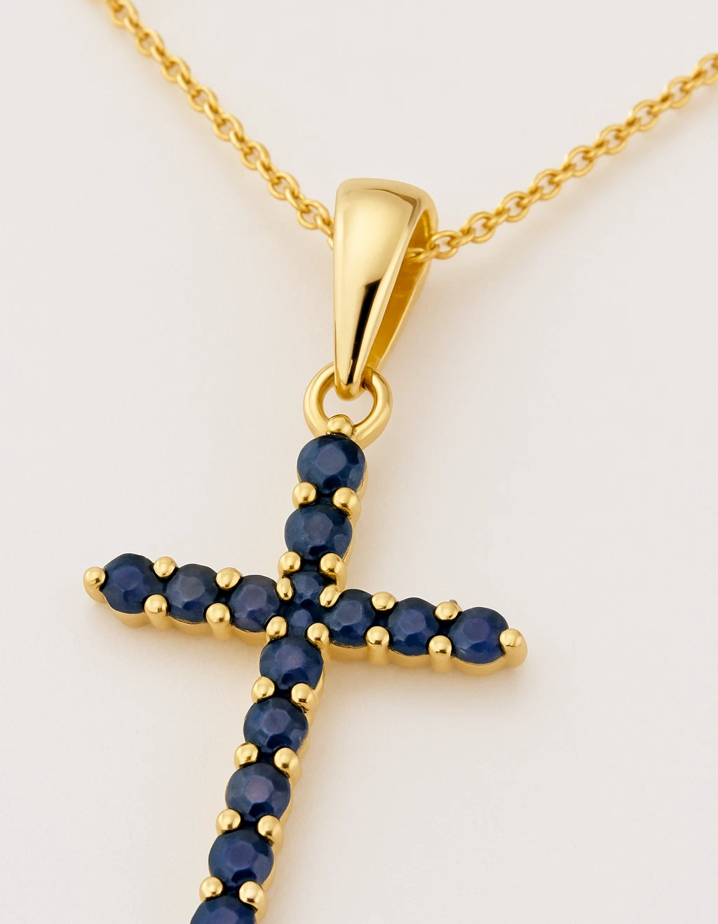 Gold cross pendant with blue stones on a gold chain against a white background