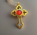 Gold cross pendant with a red gemstone on a gray background