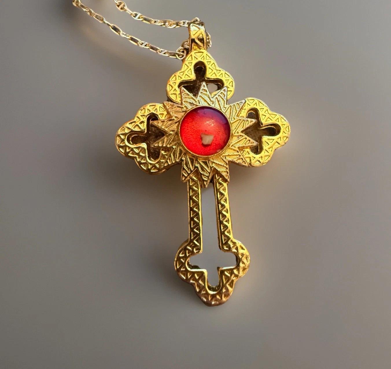 Gold cross pendant with a red gemstone on a gray background