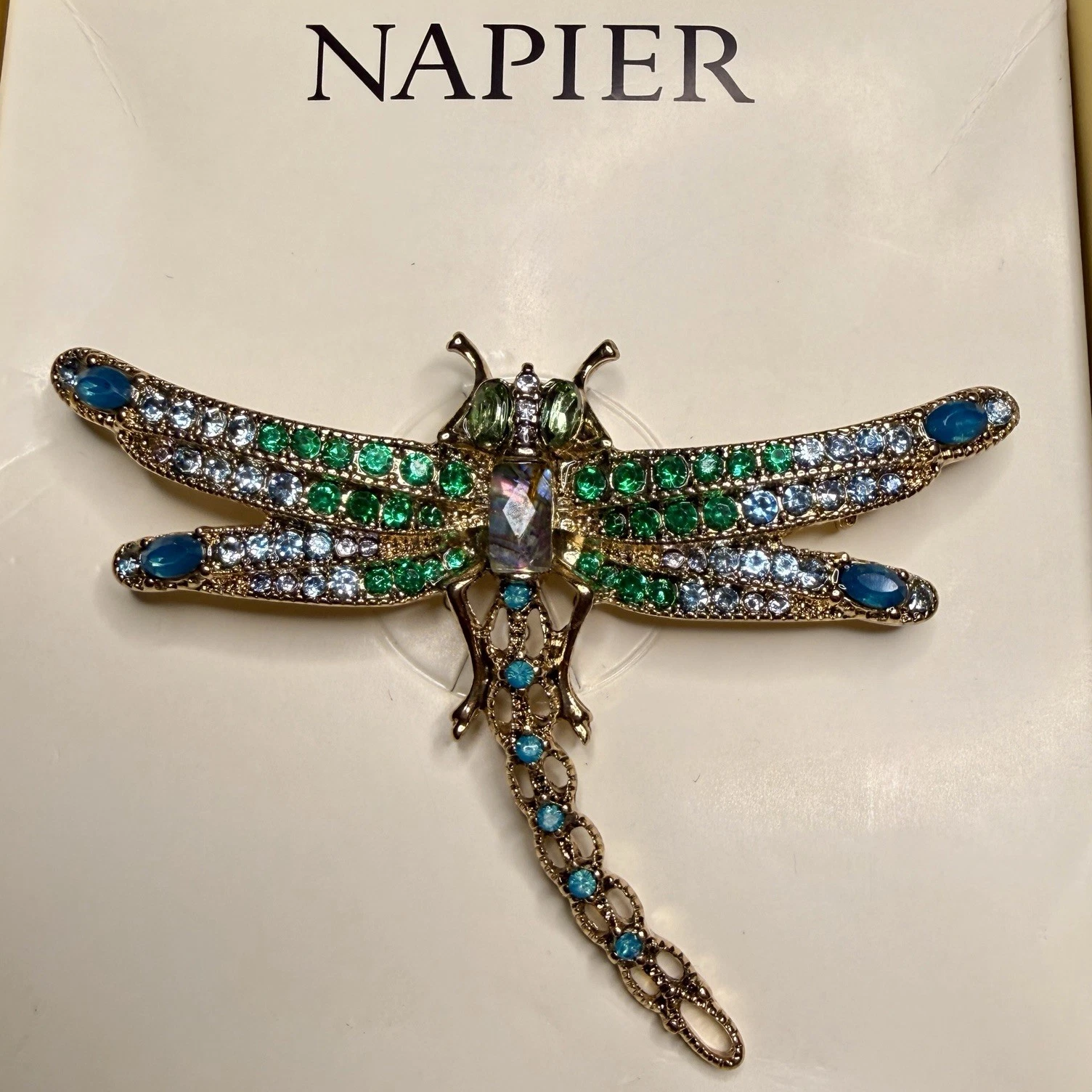 Jeweled dragonfly brooch with green, blue, and clear stones on a Napier branded background